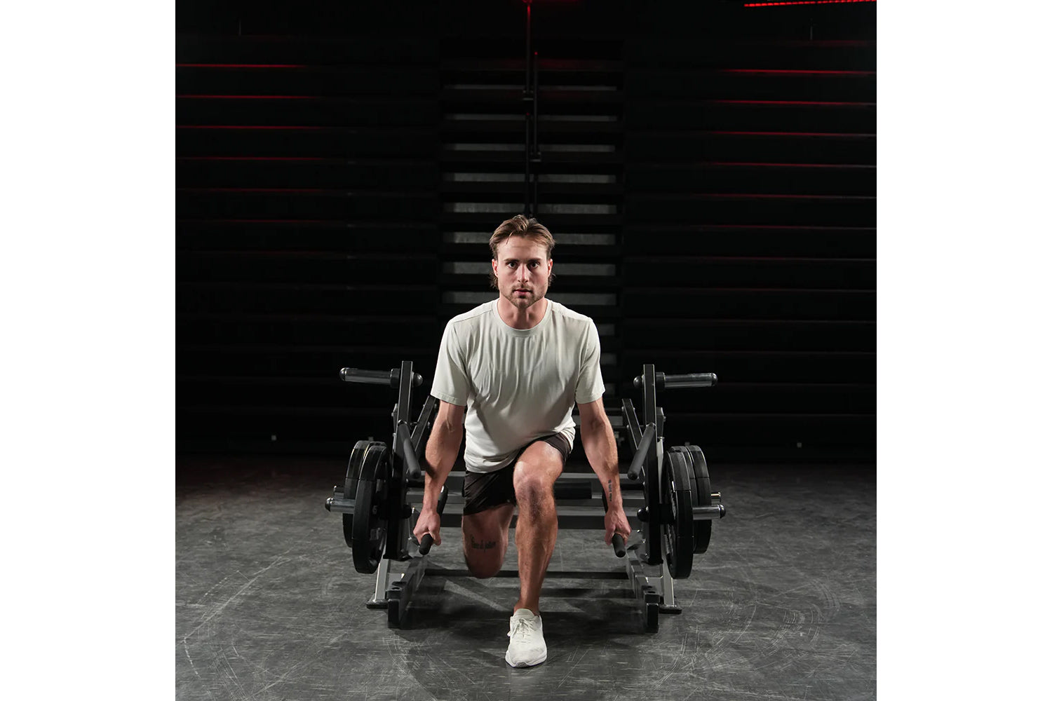 Man wearing sage green t-shirt and black shorts performing squat exercise on Hammer Strength Ground Base Multi-Squat Machine 