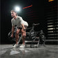 Man in light gray t-shirt and shorts using Hammer Strength multi-squat machine with black weight plates in gym setting with r