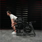 Man performing squat exercise on Hammer Strength Ground Base Multi-Squat Machine with black 45-pound weight plates in gym set