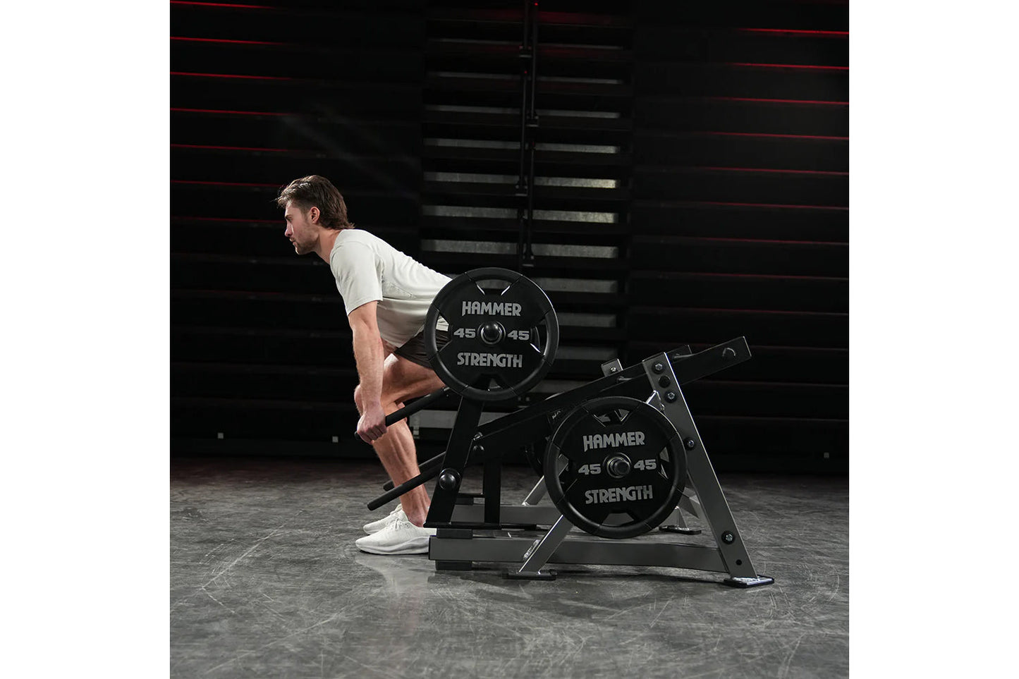 Man performing squat exercise on Hammer Strength Ground Base Multi-Squat Machine with black 45-pound weight plates in gym set