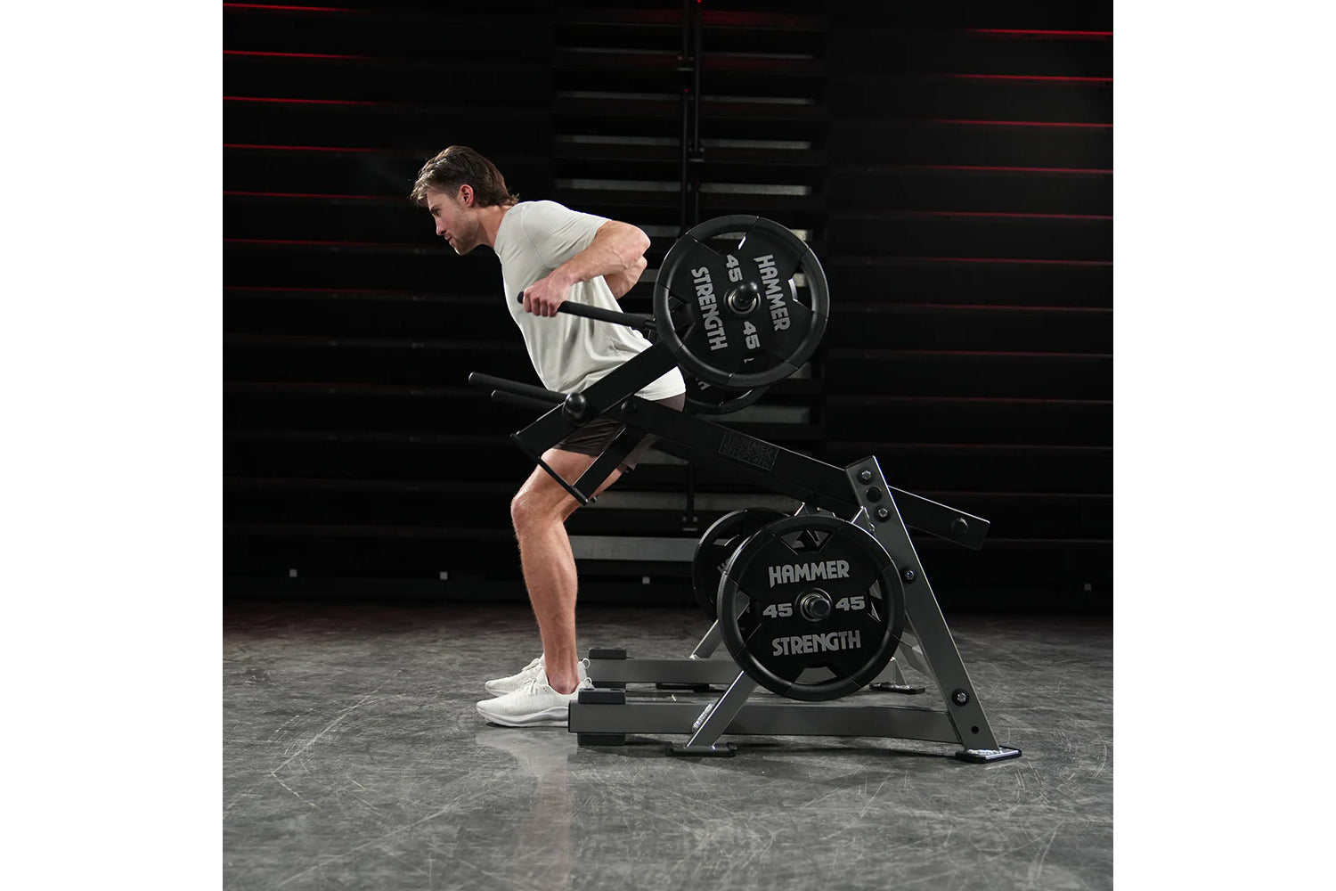 Man in gray tank top and black shorts performing squat exercise on Hammer Strength black multi-squat machine with loaded weig