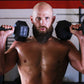 Muscular man holding black hex dumbbells at shoulder height in gym setting