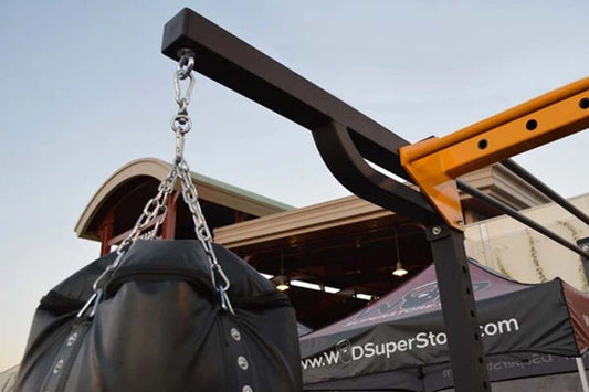 Black heavy bag suspended by silver chain from orange and black metal hoist arm apparatus