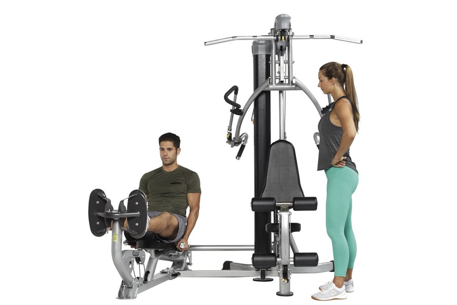 Black and silver Hoist Mi1 multi-station home gym with two models demonstrating leg press and chest press exercises