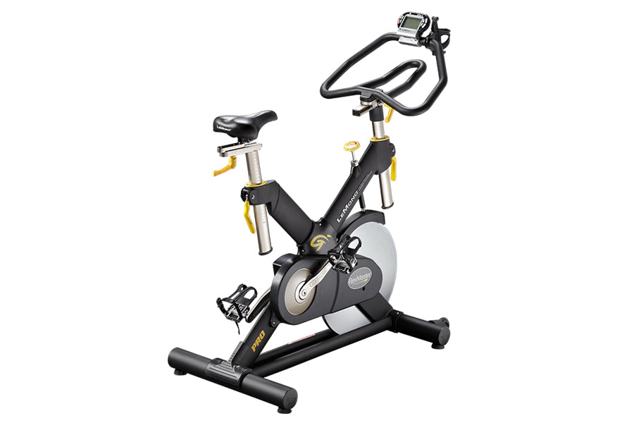 Black and silver indoor exercise bike with yellow accents, digital display on handlebars, and wide base on white background