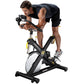 Man in black sleeveless shirt and shorts riding black and white indoor stationary bike with yellow accents on white backgroun