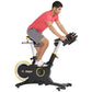 Man in coral t-shirt and gray shorts riding black and yellow Hoist stationary exercise bike with handlebar weights