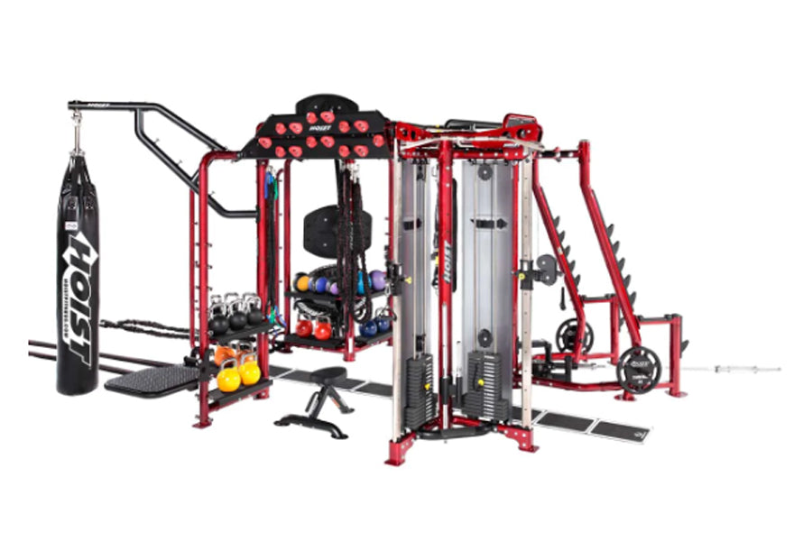 Hoist MC-7000 Series red and black multi-station gym equipment with punching bag, weight stack machines, and dumbbells on whi