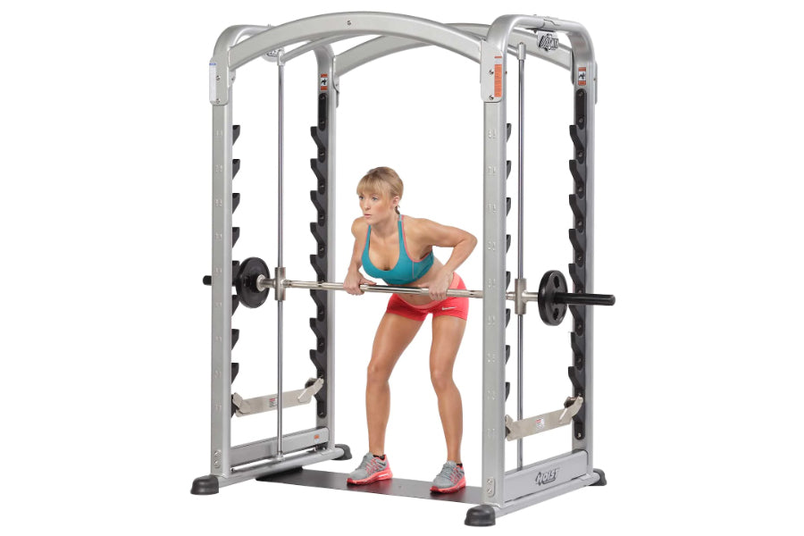 Silver and black dual action Smith machine with woman in teal top and pink shorts performing barbell exercise, on white backg