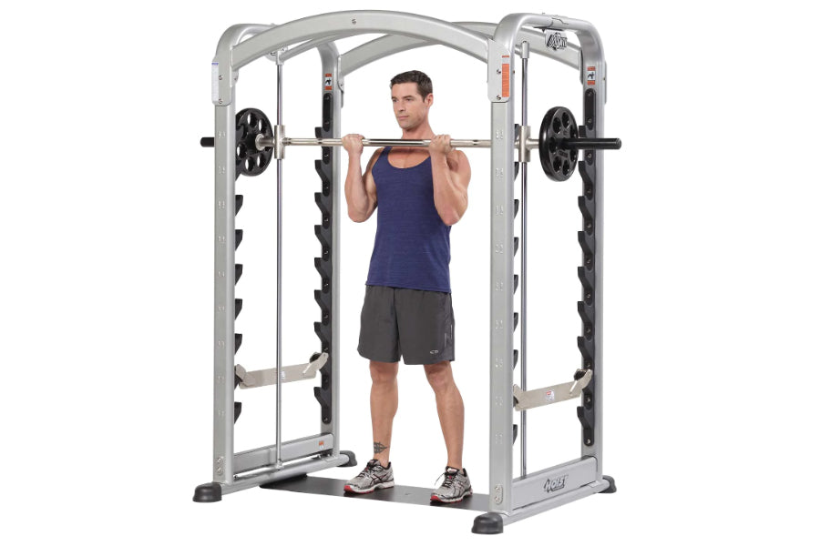 Silver and black dual action Smith machine with male model demonstrating squat position holding barbell