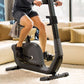 Person using black Horizon upright exercise bike in living room with cream sofa and gold pillows