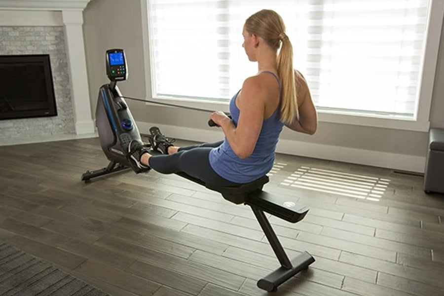 Woman using black Horizon Oxford 6 rowing machine with digital display, worn in home gym setting