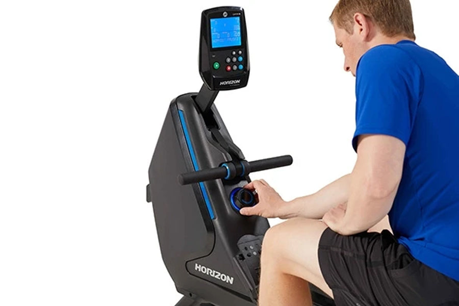 Man in blue shirt using black and blue Horizon stationary exercise bike with digital display on white background