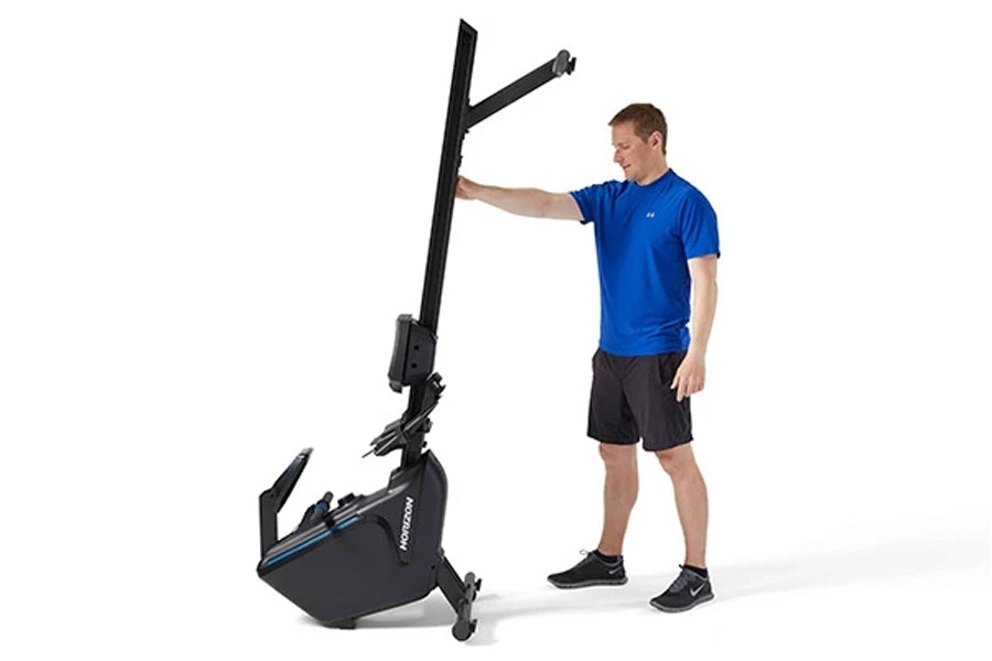 Black and blue Horizon Oxford 6 rowing machine with tall vertical frame, shown with male model in blue shirt demonstrating us