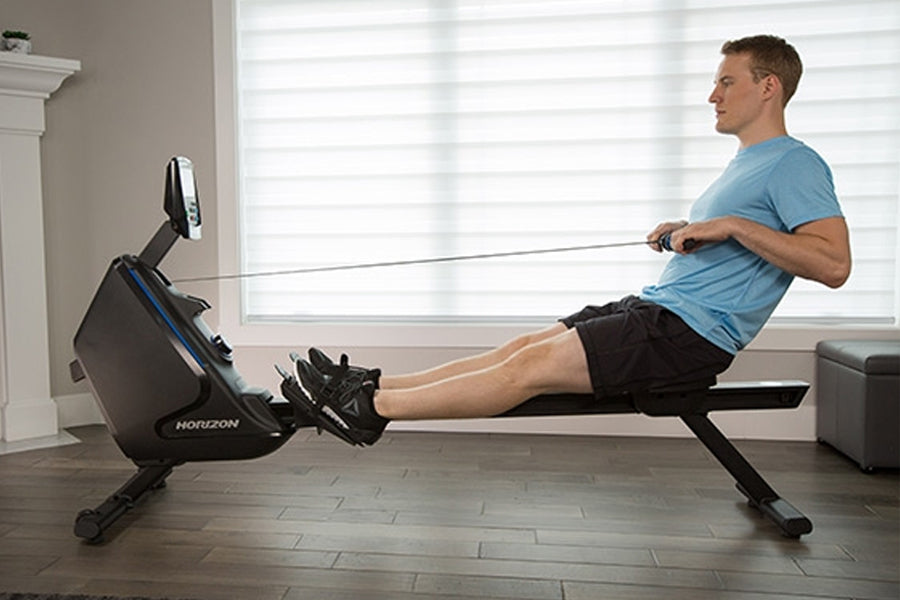 Man in blue t-shirt and black shorts using black and blue Horizon Oxford 6 rowing machine in home gym with bright windows