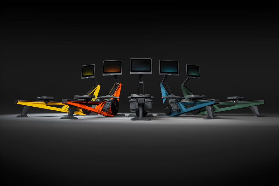 Collection of five Hydrow Wave rowing machines in yellow, orange, black, blue, and green with digital screens displayed on bl