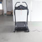 Black motorized treadmill with digital display console and curved handles, shown on warehouse floor