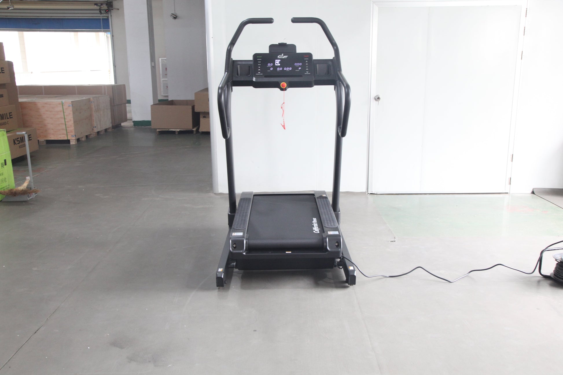 Black motorized treadmill with digital display console and curved handles, shown on warehouse floor