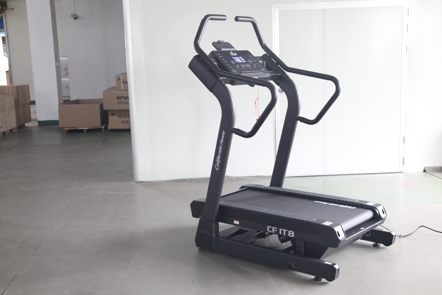 Black motorized treadmill with digital console display and curved handles, on concrete floor in warehouse setting