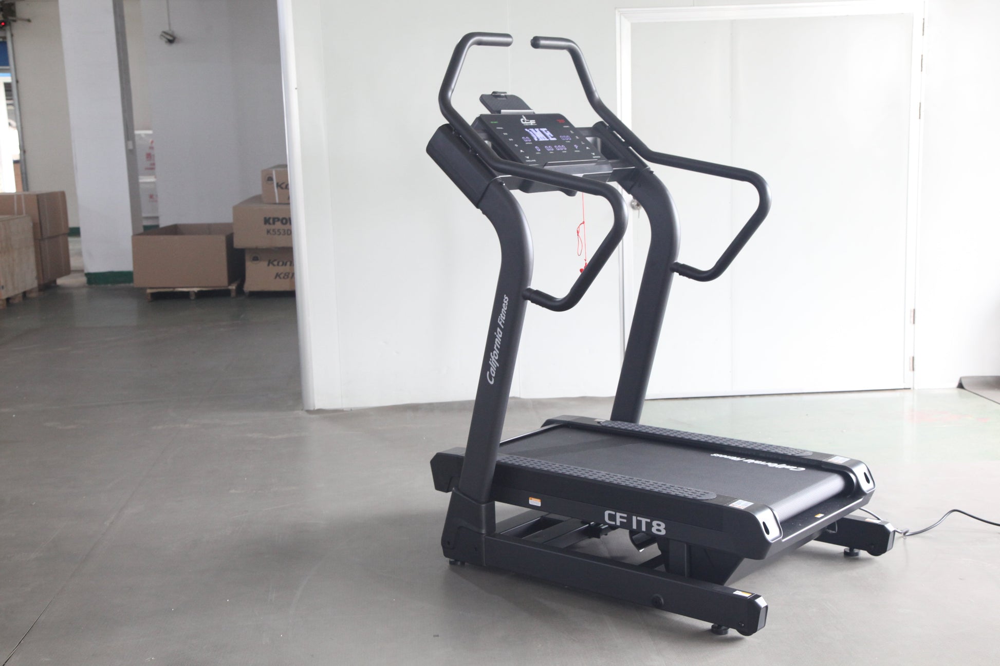 Black motorized treadmill with digital console display and curved handles, on concrete floor in warehouse setting