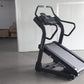 Black motorized treadmill with digital display console and curved handrails, displayed in warehouse setting