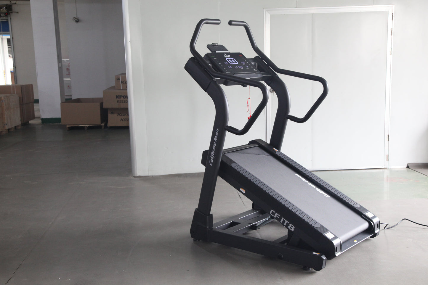 Black motorized treadmill with digital display console and curved handrails, displayed in warehouse setting