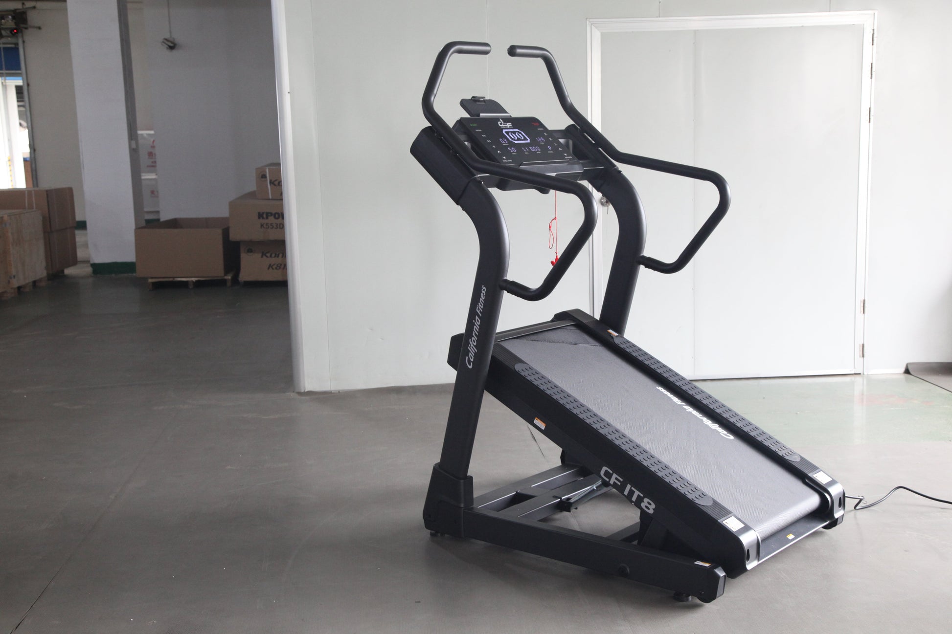 Black motorized treadmill with digital display console and curved handrails, displayed in warehouse setting