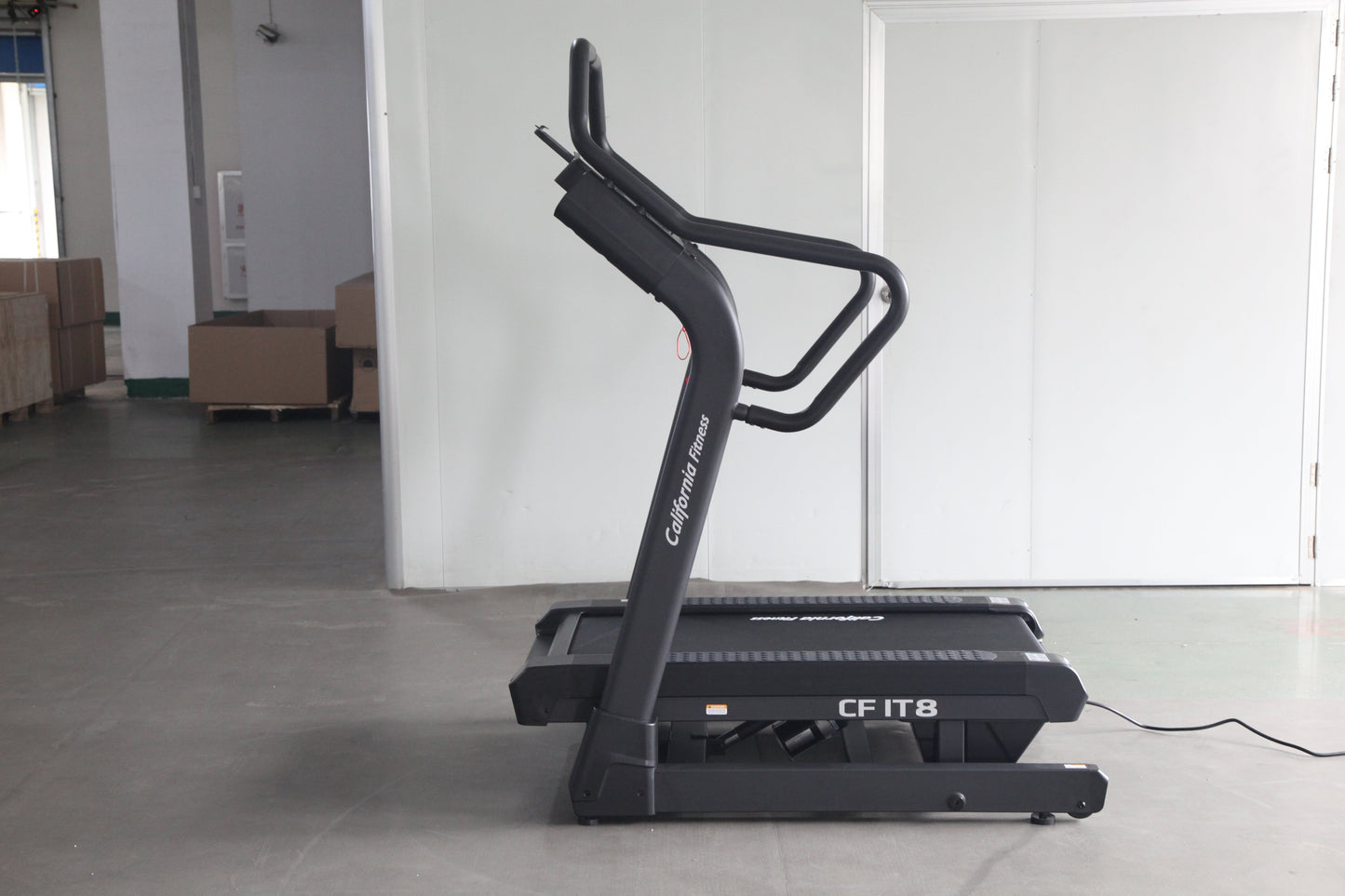 Black treadmill with curved running deck and dual handles labeled "CF IT8" on concrete floor in warehouse setting