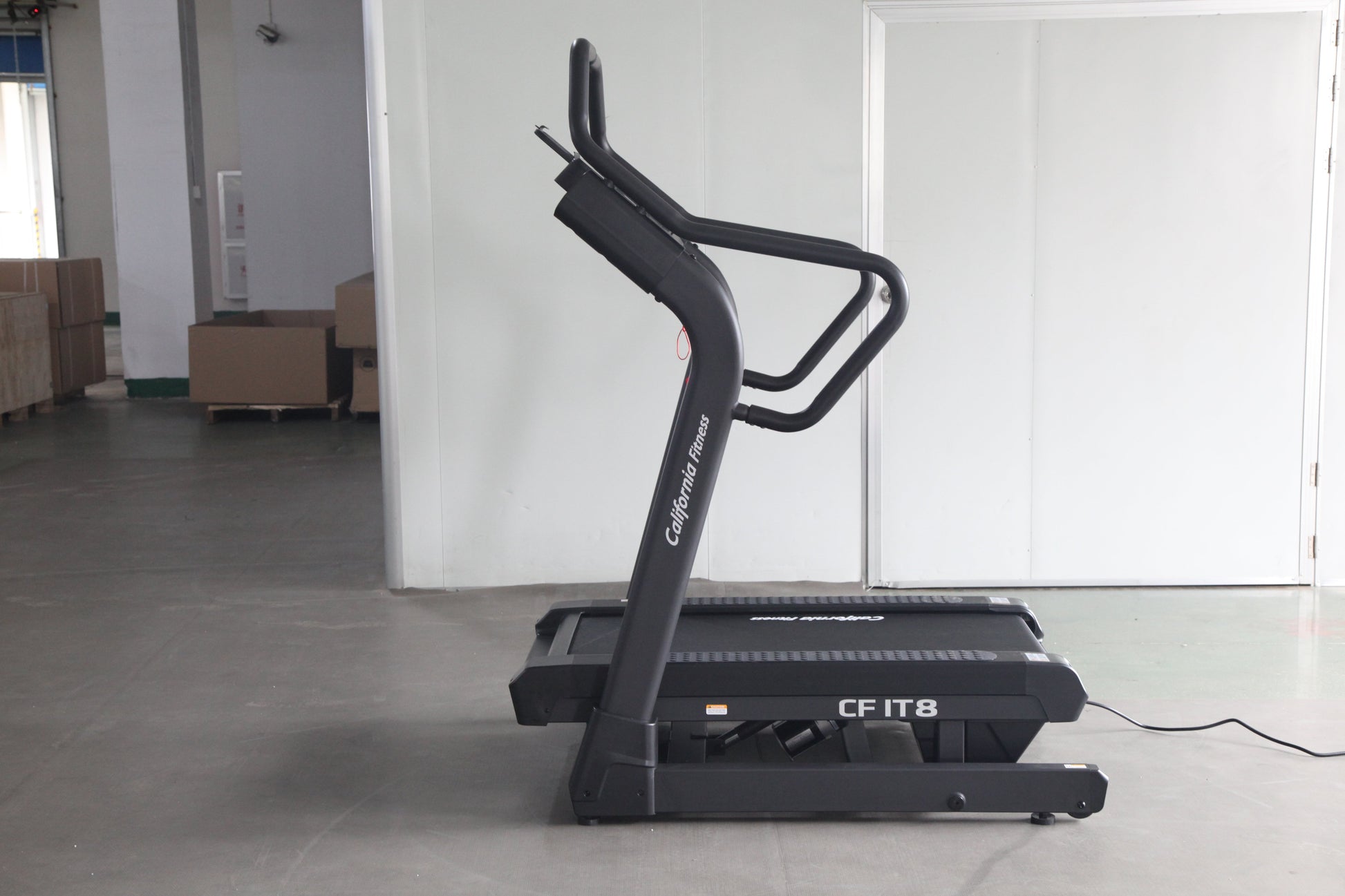 Black treadmill with curved running deck and dual handles labeled "CF IT8" on concrete floor in warehouse setting