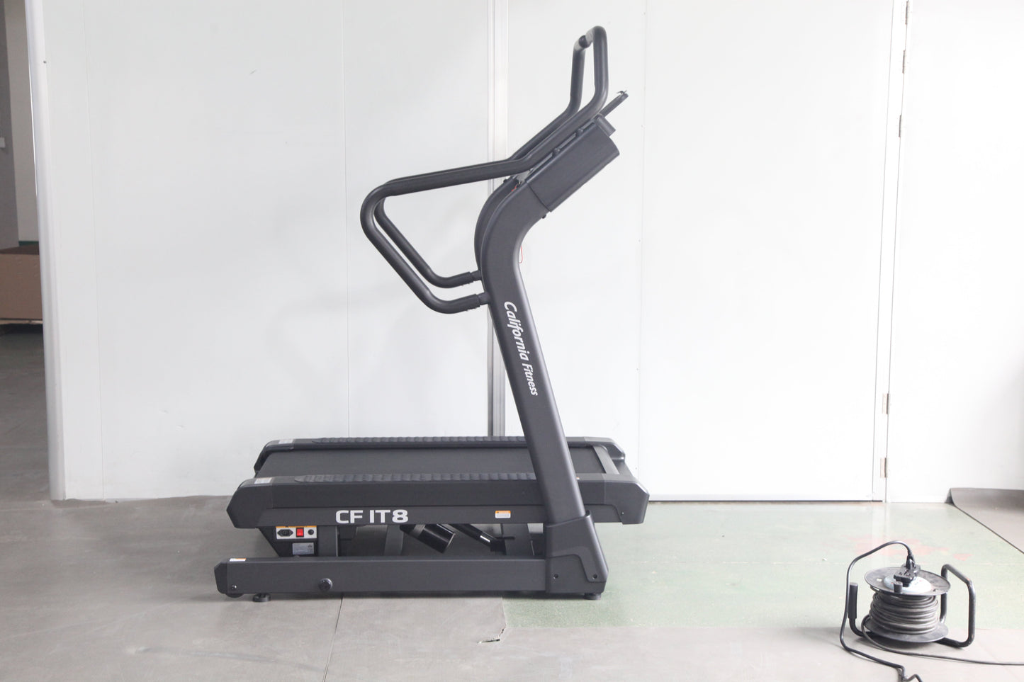 Black motorized treadmill with curved running deck and dual handlebar grips, model CF IT8, on white background with power cor