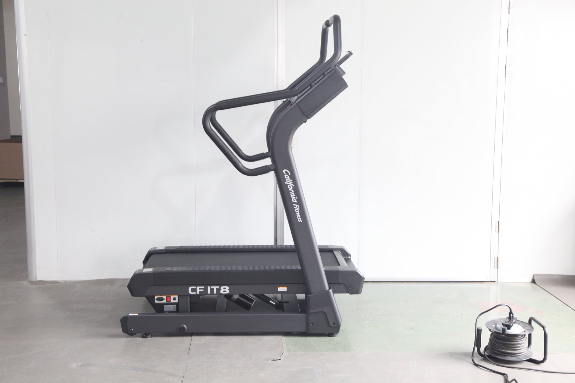 Black motorized treadmill with curved running deck and dual handlebar grips, model CF IT8, on white background with power cor