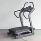 Black motorized treadmill with digital control panel and curved handles, on concrete floor against white wall
