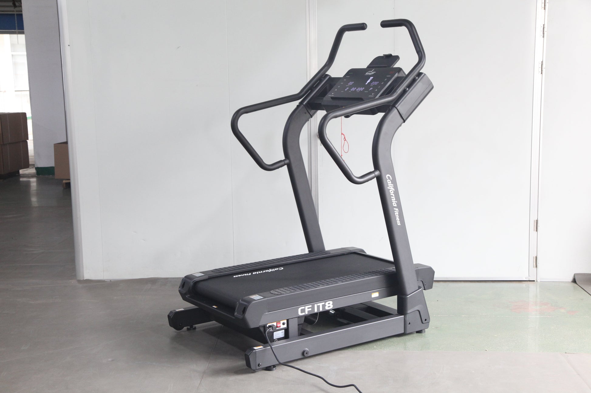 Black motorized treadmill with digital control panel and curved handles, on concrete floor against white wall