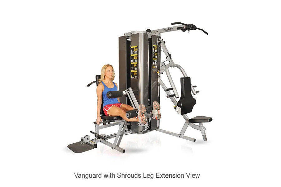 Woman using silver and black multi-gym with leg extension attachment, demonstrating exercise position on fitness equipment
