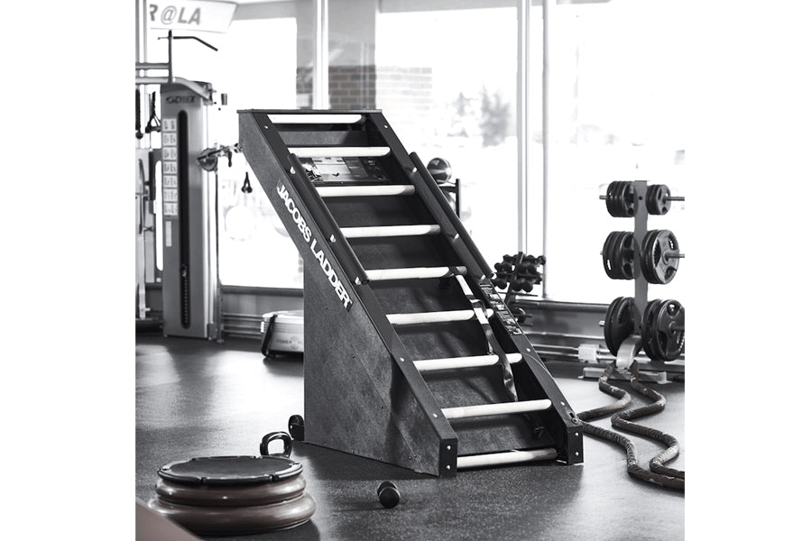 Black Jacobs Ladder climbing machine with white grip steps in gym setting with weights and equipment visible