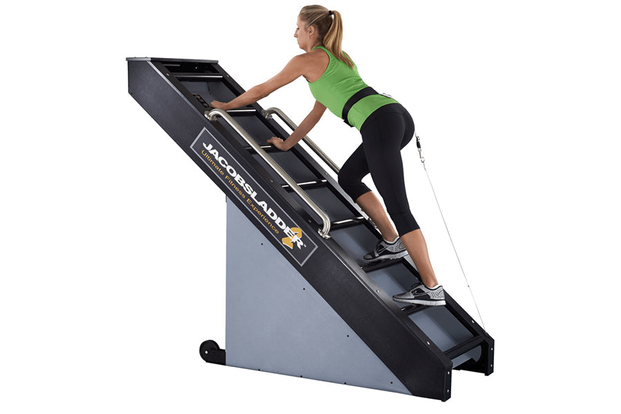 Woman in green sports bra and black leggings using black and gray Jacobs Ladder 2 climbing machine against white background