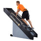 Man in orange shirt and black shorts climbing on black and gray Jacobs Ladder 2 exercise machine against white background