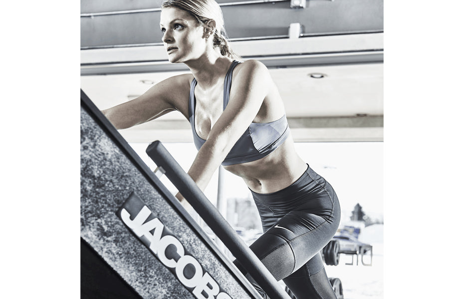 Woman in blue sports bra and black shorts using Jacobs Ladder climbing machine in gym