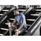 Man in blue t-shirt and black shorts climbing on Jacobs Ladder machine in gym setting, holding white water bottle