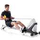 Man using white and black indoor rowing machine with yellow resistance band, wearing black Nike shirt and shorts on white bac