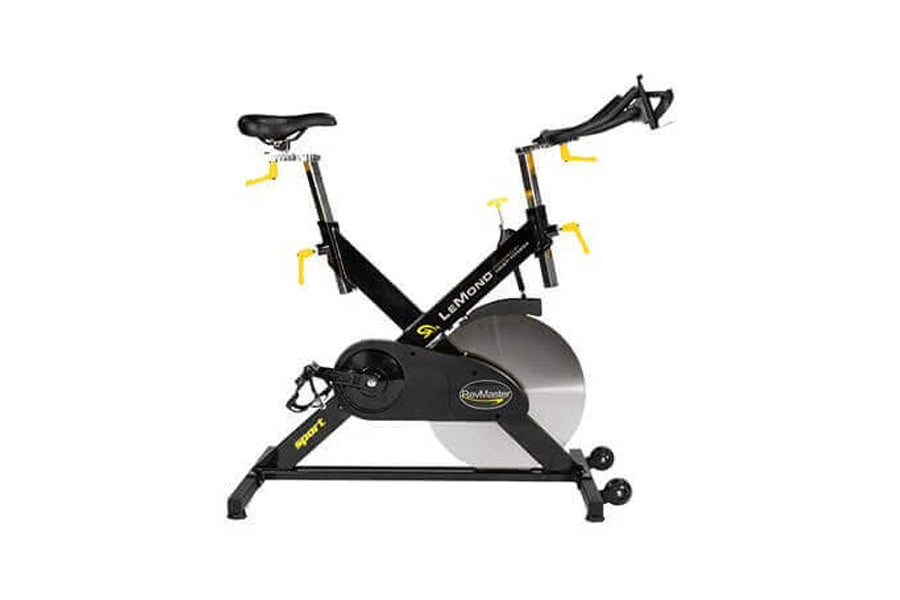 Black and yellow indoor exercise bike with drop handlebars, adjustable seat, and large flywheel, front view on white backgrou