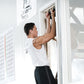 Man wearing white tank top and black pants using black portable chin up grips on doorway frame