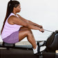 Woman in lavender tank top and purple shorts using black rowing machine on white background