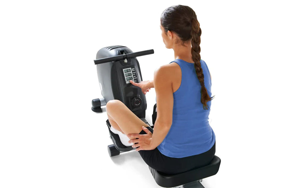 Woman using black and silver stationary exercise bike with digital display console on white background