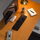 Overhead view of wooden desk with black keyboard, monitor, ceramic mug, notepad, brass lamp, and power strip showing under-de