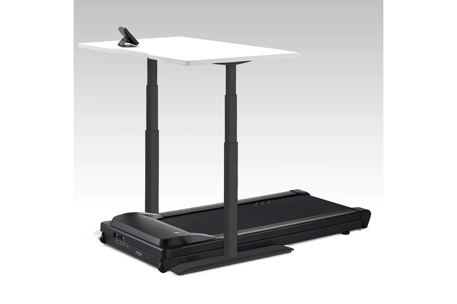 Adjustable standing desk with white tabletop and black metal frame mounted over black power treadmill, displayed on gray back