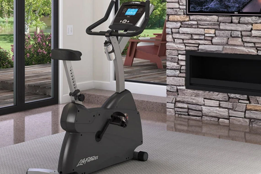 Black and silver upright exercise bike with blue display console in home gym setting with fireplace
