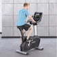 Man in blue t-shirt and black shorts riding black and silver upright stationary bike with digital display console, gray tile 