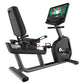 Black recumbent exercise bike with gray frame, padded seat, attached tablet displaying fitness content, and console controls