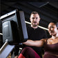 Two people using black recumbent exercise bike in modern gym setting with overhead lighting